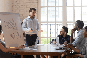 People in an office setting with one person standing at a whiteboard presenting