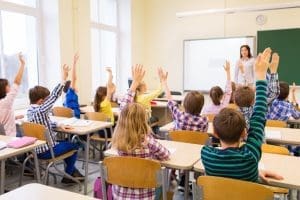 Students sitting in a classroom raising their hands