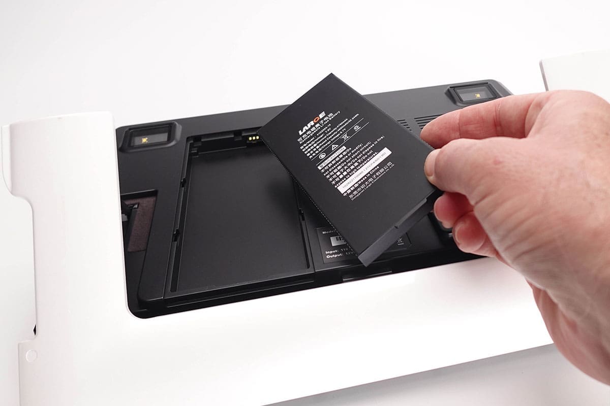 A hand is removing a black battery from a device's compartment, revealing the internal structure.